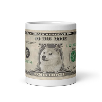 Image of a white ceramic mug featuring the 'Doge Bill' design. The design mimics a U.S. one-dollar bill but replaces George Washington with the iconic Shiba Inu Doge meme. The text on the mug reads 'DOGECOIN RESERVE NOTE' at the top, 'TO THE MOON' in the center, and 'ONE DOGE' at the bottom. The serial number 'L11180916G' is visible, along with the seal of the Dogecoin Reserve in green, and the word 'Internet' instead of 'Washington, D.C.' on the right side. This mug is a humorous tribute to Dogecoin